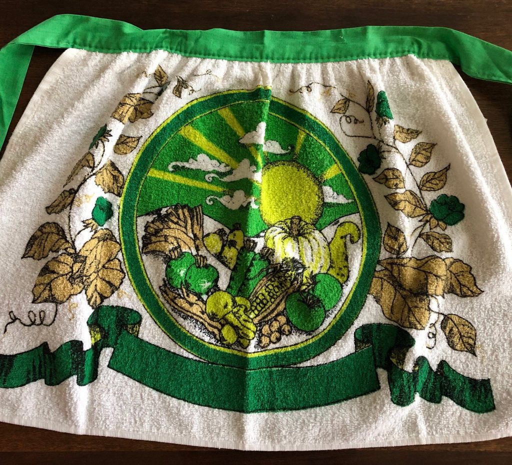 Vintage Thanksgiving: a cute terry towel cotton half apron. It has shades of green and a tan brown "Thanksgiving bounty" of fruits and vegetables with fall leaves on the edges. Circa 1960s. 