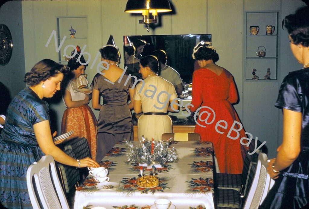 1950s photo of a group of women in fantastic 1950s dresses all gathered in the dining room during a New Years Eve party. 