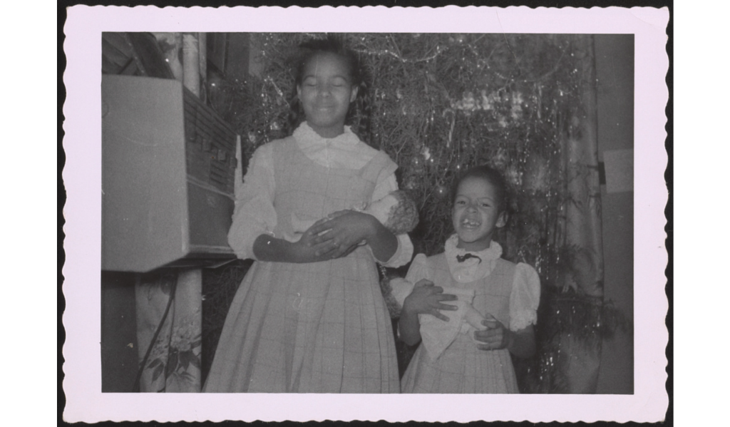 1950s / 1960s photo of 2 young Black girls holding dolls in front of the Christmas Tree