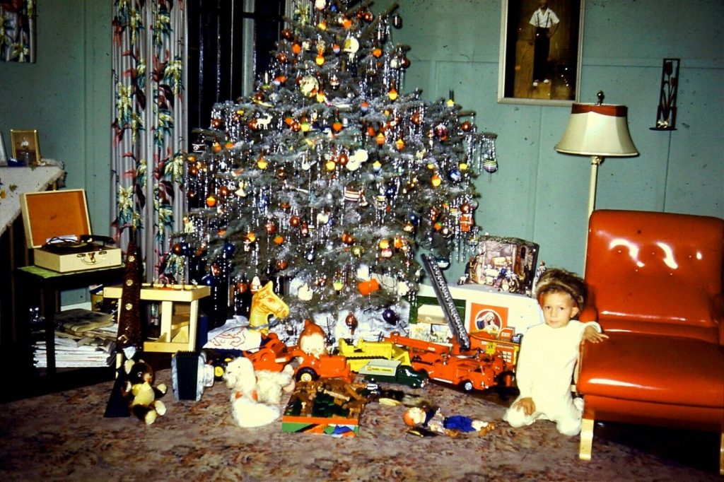 1950s vintage photo of a christmas tree with lots of toys underneath it and little child beside it.