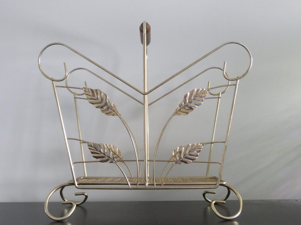 A wonderful mid century modern vintage find! This brass magazine rack with a wood handle. The basket of the rack is open with leaft detail, a performated metal base and scrolled feet and scrolled metal along the top. Is great for storage or home organziation