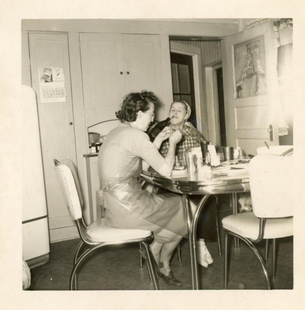 2 ladies sharing a meal and a drink together at the chrome kitchen table circa 1950s vintage photo.