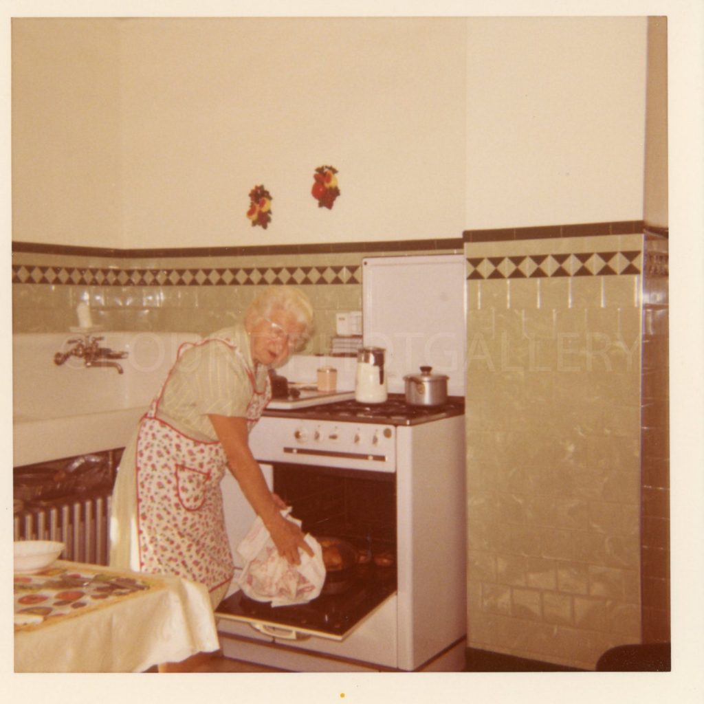 1950s Photo (I believe) of a Grandmother taking a turkey out of the oven in her classic kitchen that features green depression era tiles.