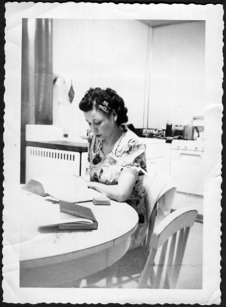 1950s vintage photo of a woman at her kitchen table reading a book with a piece of her hair in curlers