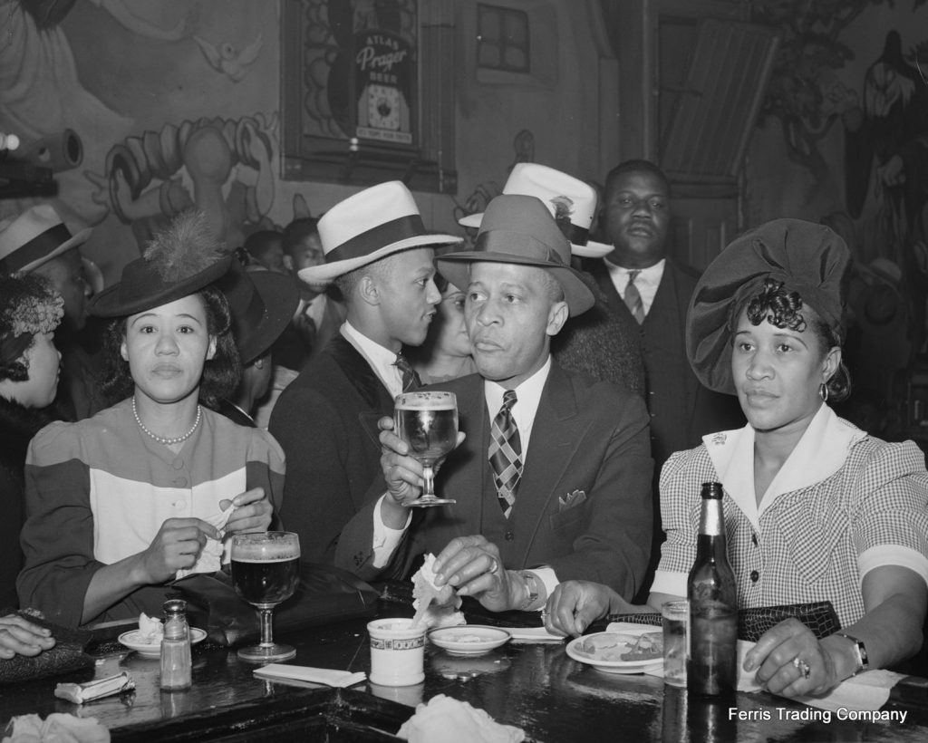 1940s photo of Black Men and Black Women in stylish 1940s fashions enjoying beers and food in Harlem