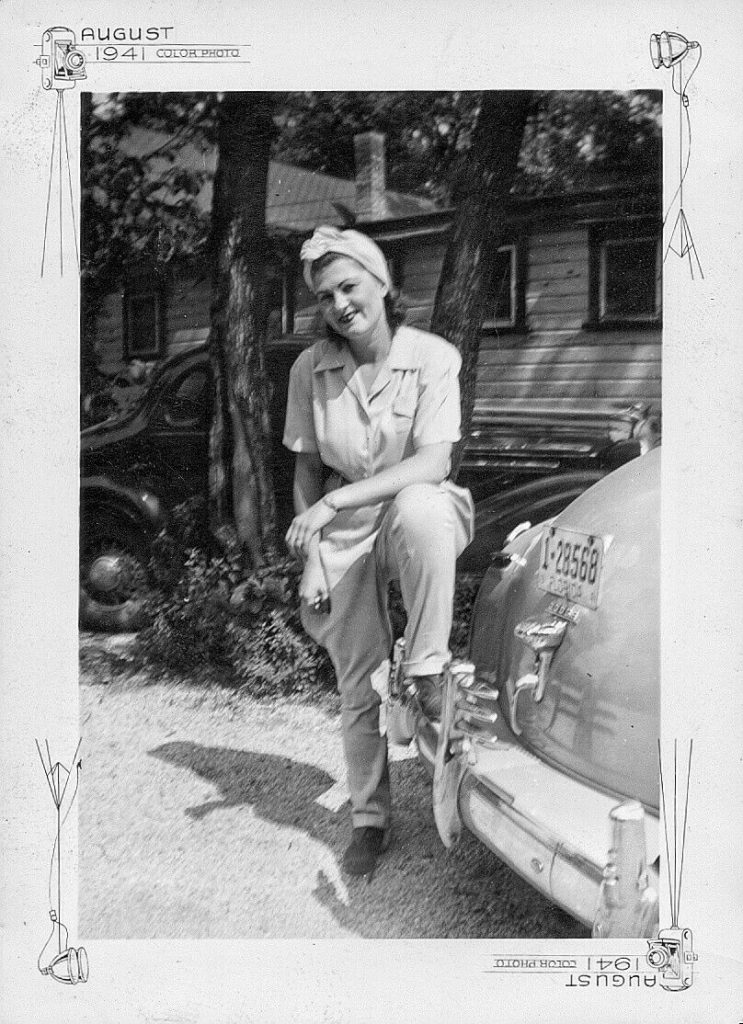 1940s vintage photo (August 1941) of a woman in a Hair Turban, pants, blouse and posing on the bumper of a car. 