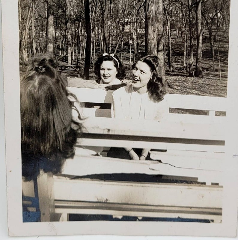 1940s photo of 3 women sitting on park benches having some together wearing cute 1940s hairstyles