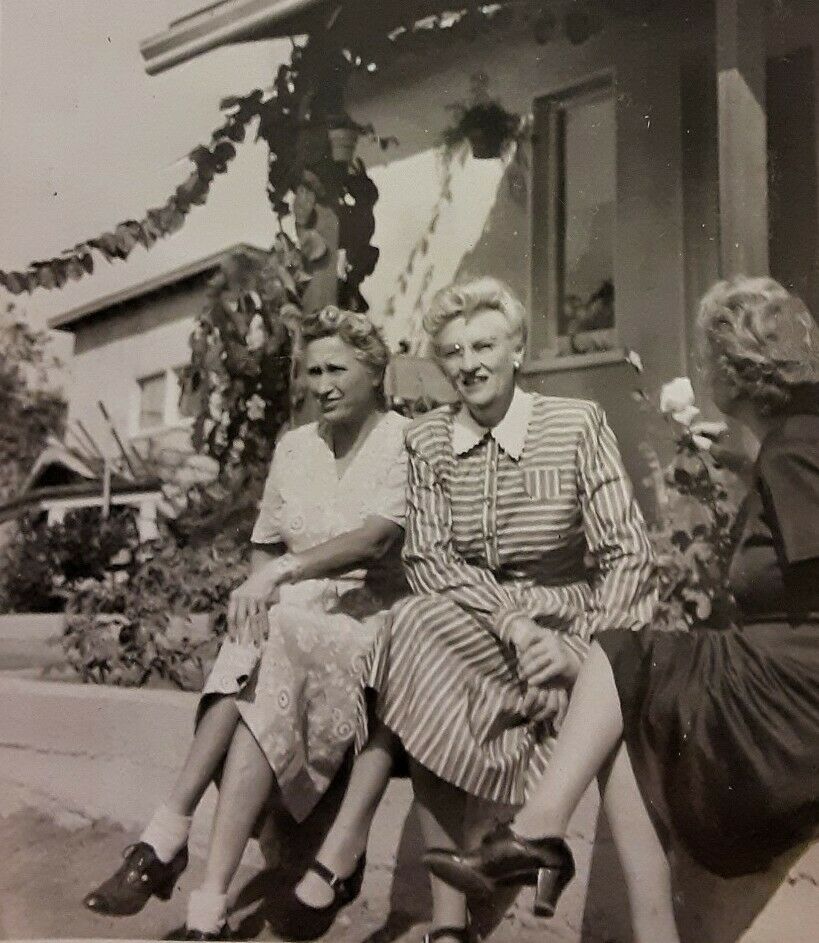 1940s vintage photo of older women chatting in the front of a house together in 1940s fashions