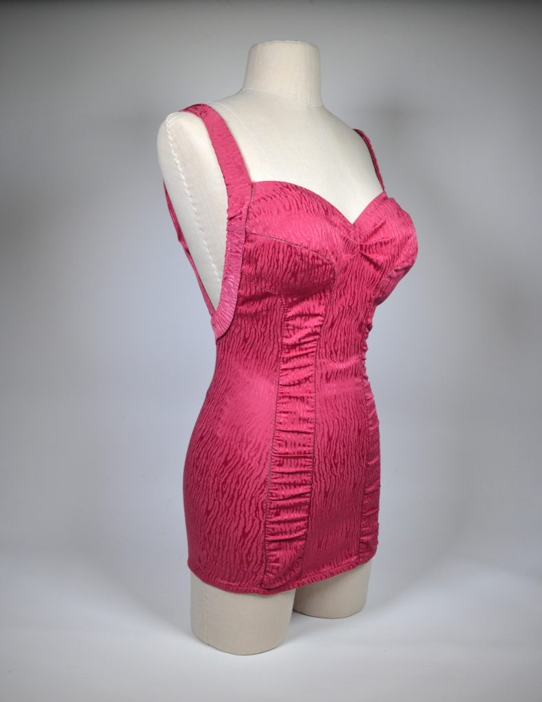 This photo shows a "Shirred Panel Classic" Rose Marie Reid swimsuit from 1951 in the Cherry Cordial color owned by the Harold B. Lee Library of Brigham Young University displayed on a dressform.