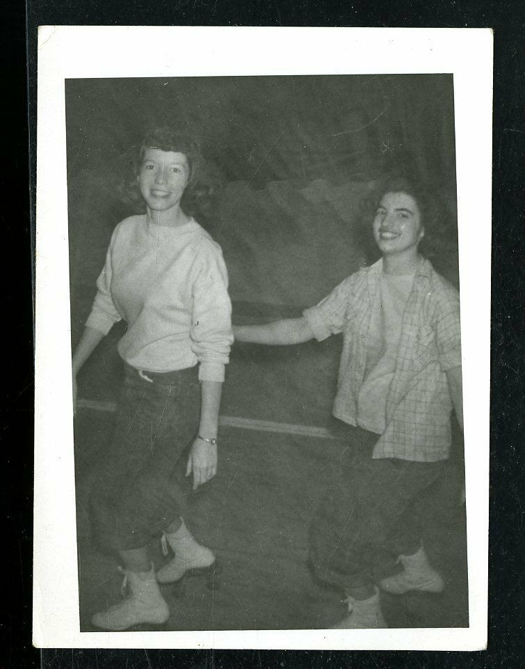 1940s vintage photo of 2 girls in 1940s fashion (jeans and tops) roller skating together. 