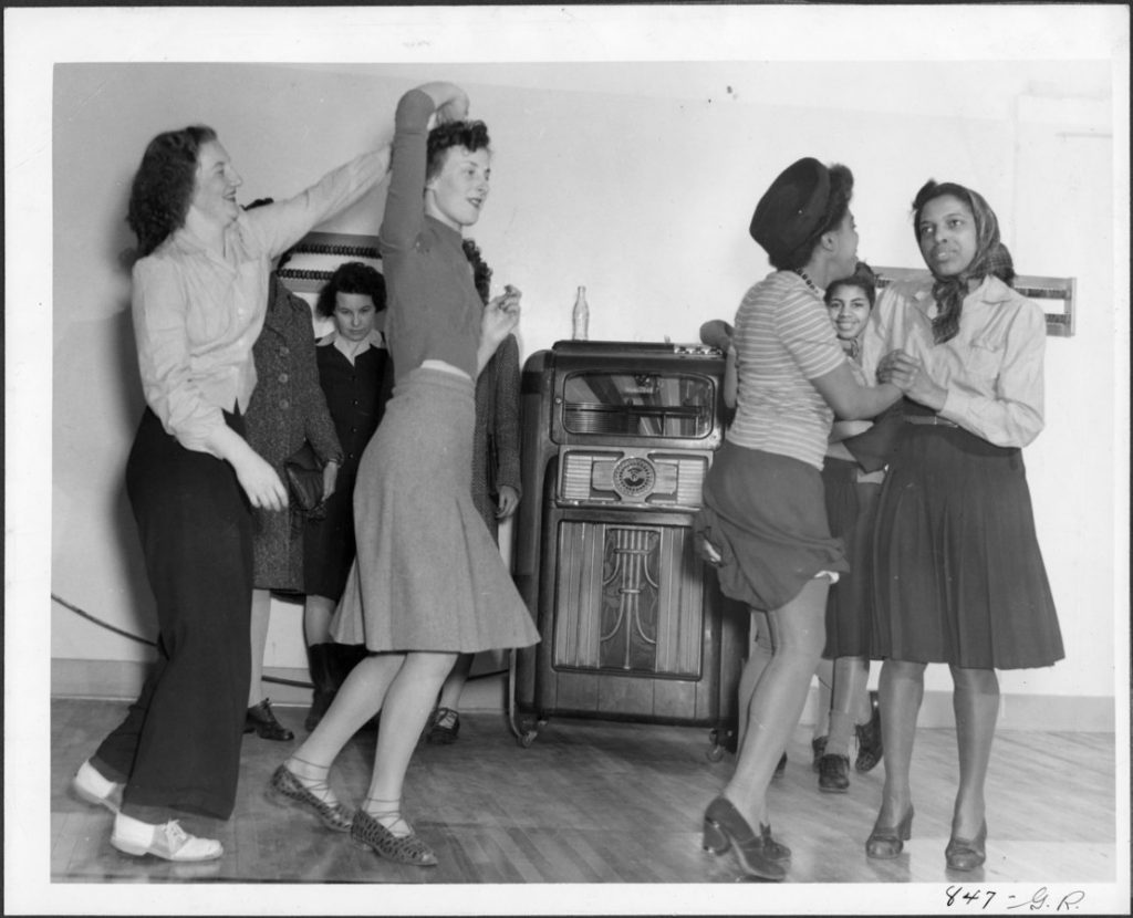 1940s vintage photo of Black Women and White Women sharing a dance floor together in 1940s fashions and swing dancing. 