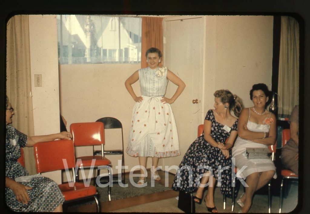 1950s 35mm amateur photo slide house party of a lady in dress from the 1950s and other women looking on.
