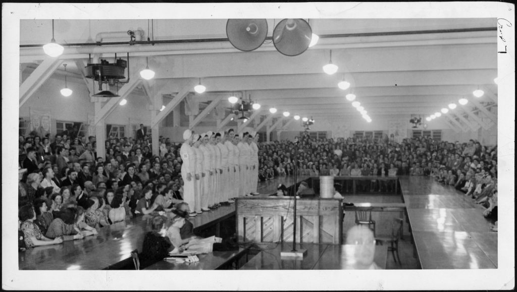 Miss War Worker Finals" - "Fusilier July 18th, 1942. Image features a group of women in their factory outfits standing in line to be judged. 