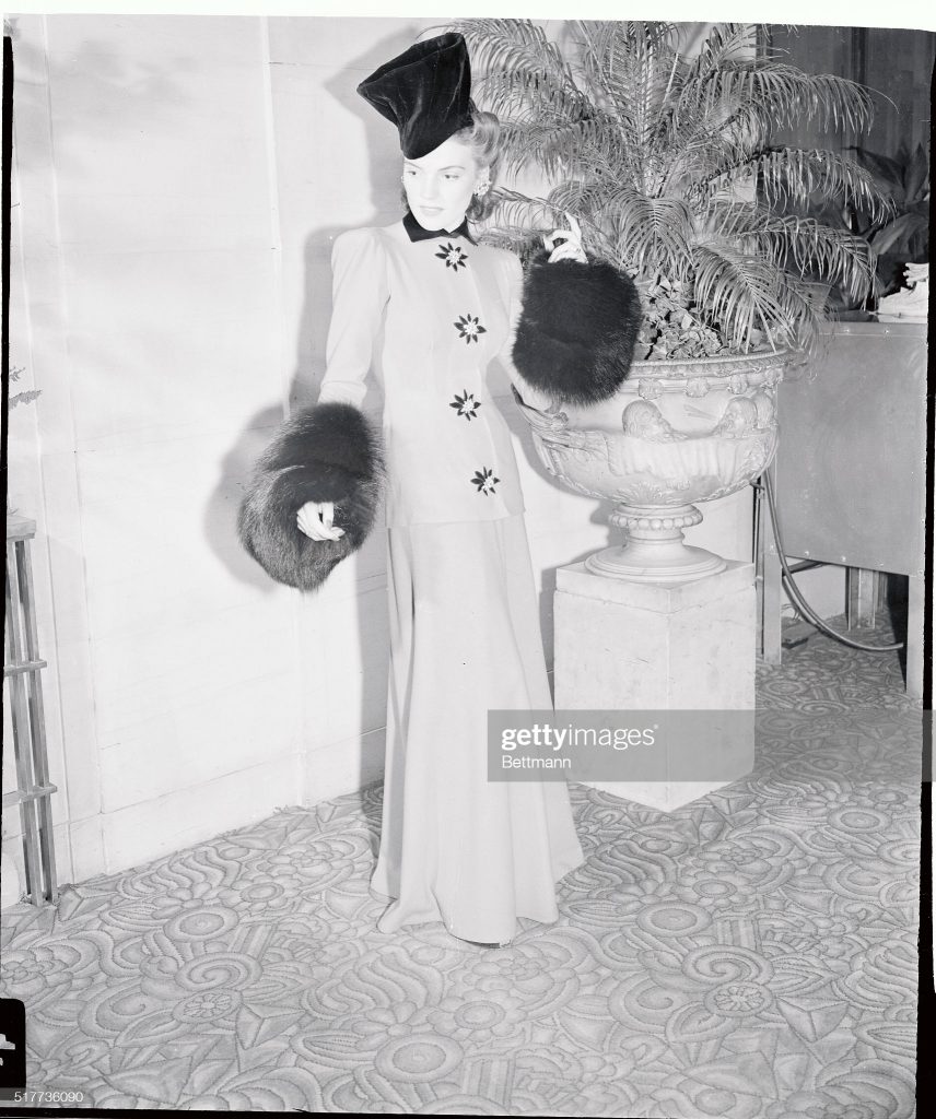 1940s Photo: 1941 vintage photo of a Model Wearing Hat and Long Suit with Fur Trim. The outfit is a Carrie Munn Design. Beautiful 1940s fashion. 
