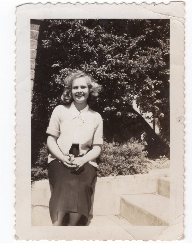 1940s Photo of a young blonde woman in a cardigan and skirt with 1940s hairstyle sitting by stairs. 