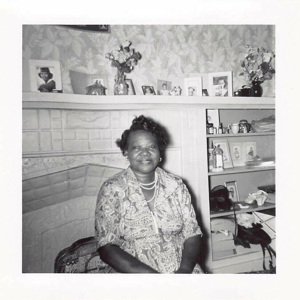 1960s photo of a Black woman seated in a living room in a pretty 1960s dress