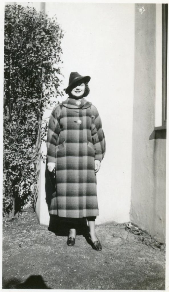 Late 1930s early 1940s photo of a young woman in a very long plaid jacket wearing a hat.