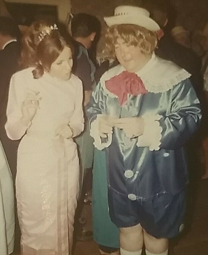 1960s vintage photo from a halloween party featuring a man dressed up as a little victorian kid and a pretty young woman in a 1960s dress. 