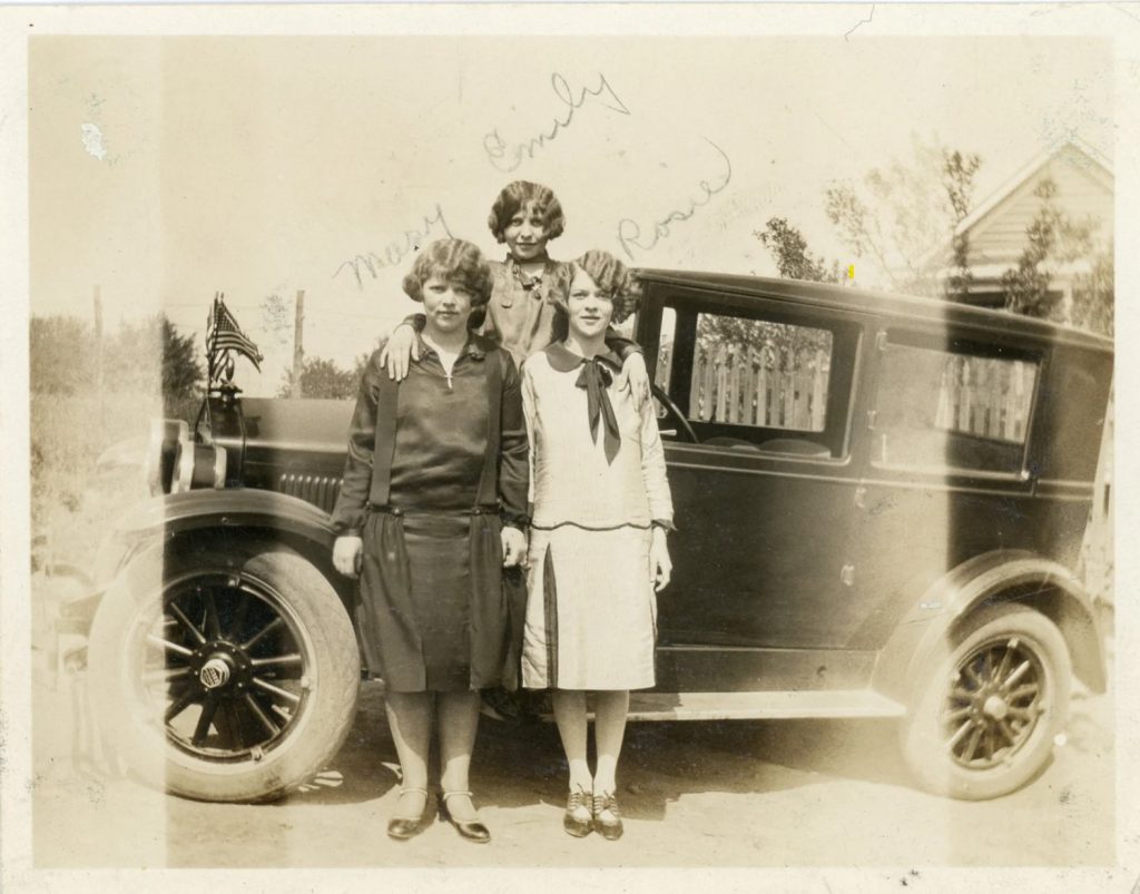 1920s vintage photo of 3 stylish women with 1920s hairstyles and 1920s dresses in front of a 1920s car