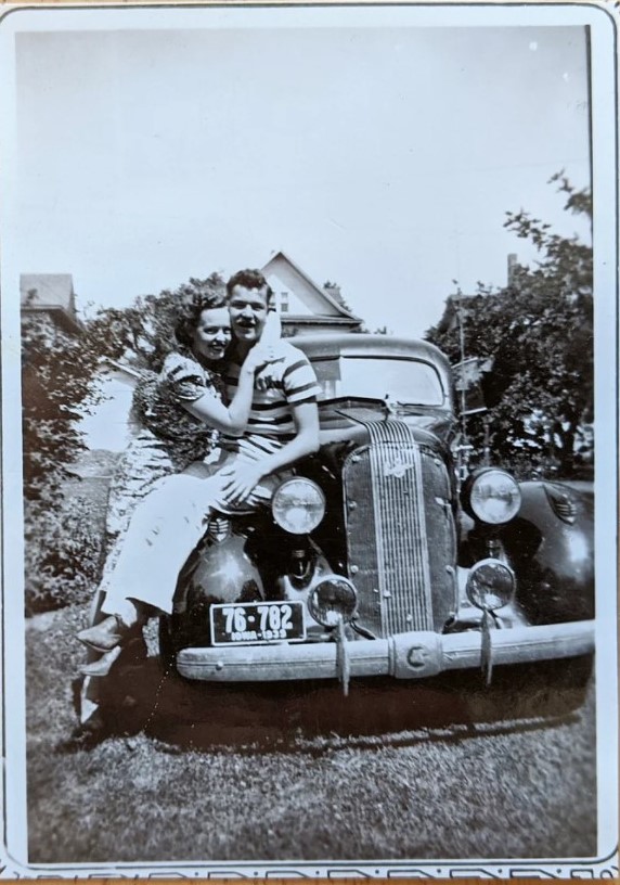 1930s vintage photo of a couple holding each other while posing on the car. 