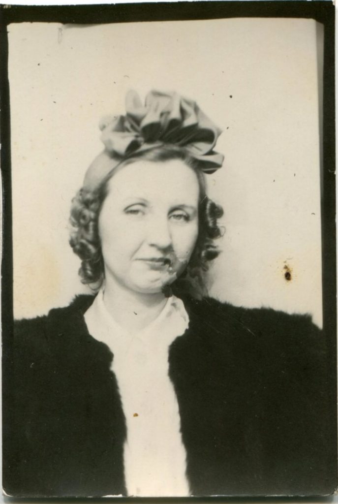 1940s vintage image of a woman in a photo booth with a 1940s hair accessory covering her hair (a headband). 