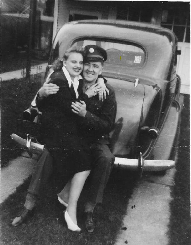 1940s vintage photo of a soldier with his girlfriend posing on the back of a car.