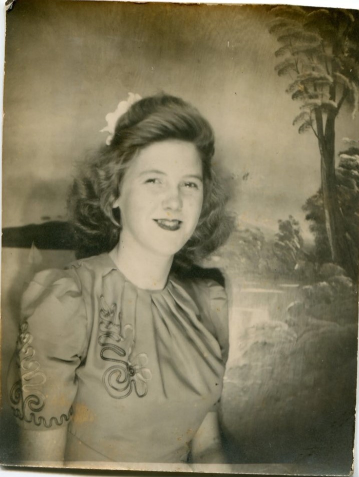 1940s vintage photo of a young woman with a 1940s hairstyle in a 1940s dress with a hair flower in her hair posing in a photobooth