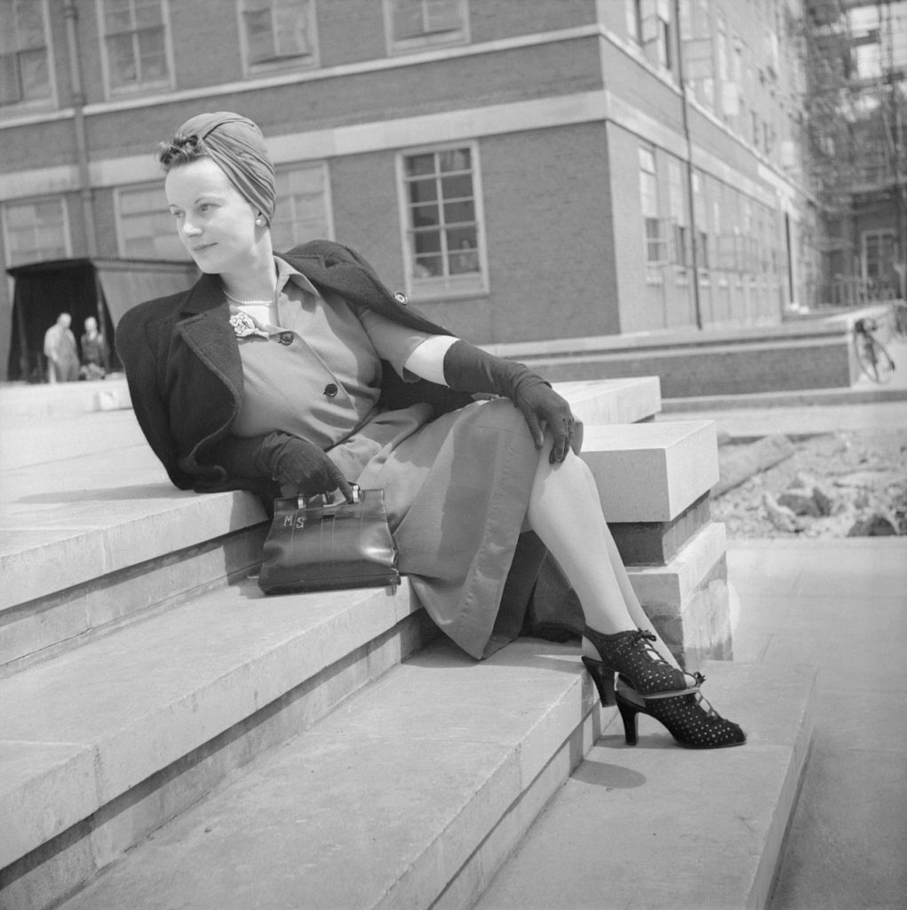 1940s Vintage Photo during WW2 of how a woman dresses during wartime. She is in a dress, 1940s turban, jackets, gloves and shoes. 