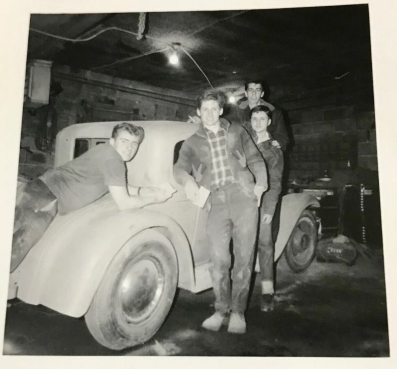 1950s vintage photo of 4 young men dressed like Greasers posing with their car in a garage