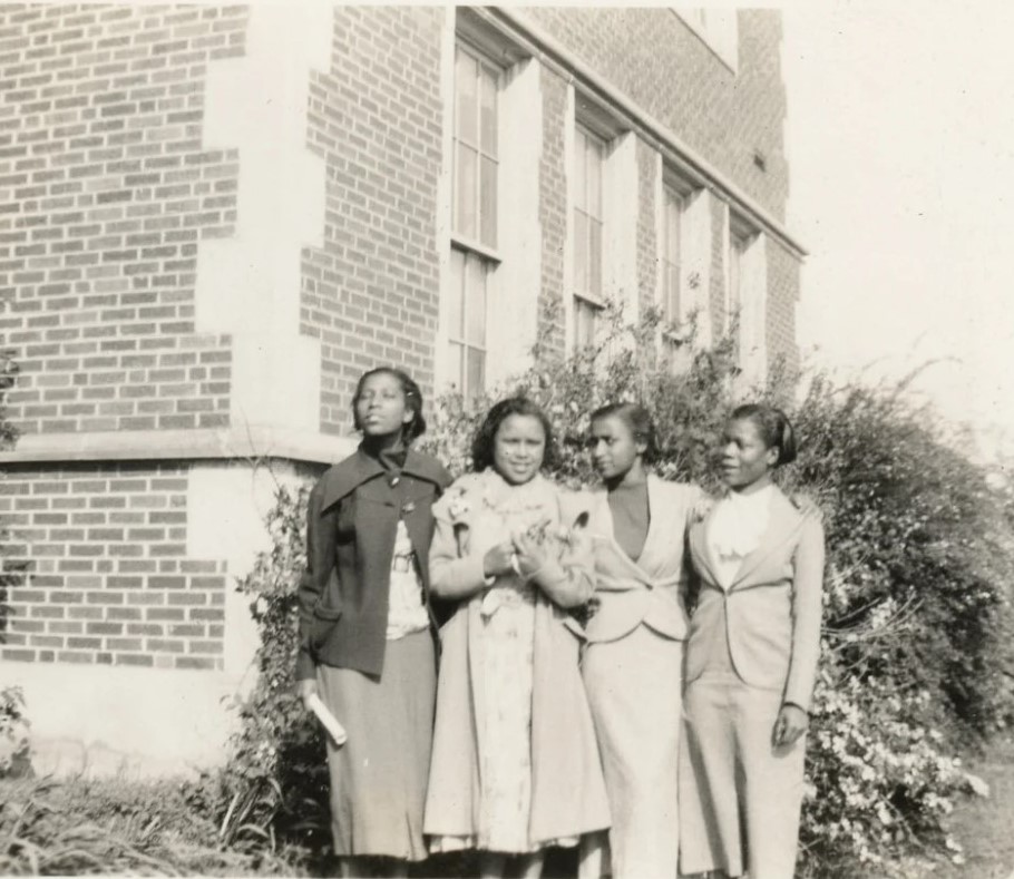 1930s vintage photo of 4 Black women posing together in 1930s fashions in front of a building. 