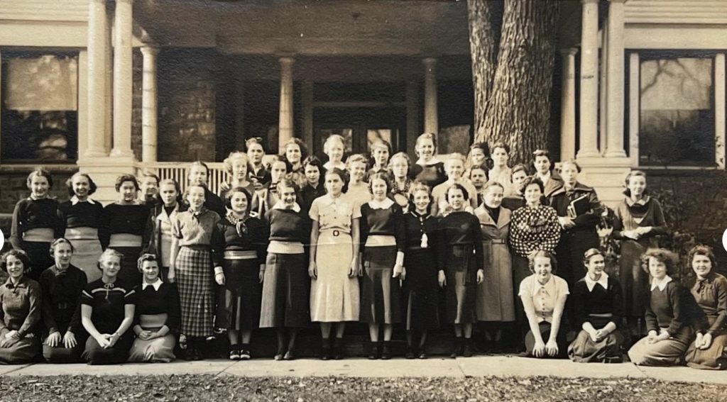 1930s vintage photo of a group of young women sorority sisters posing together in 1930s fashions in front of a house.