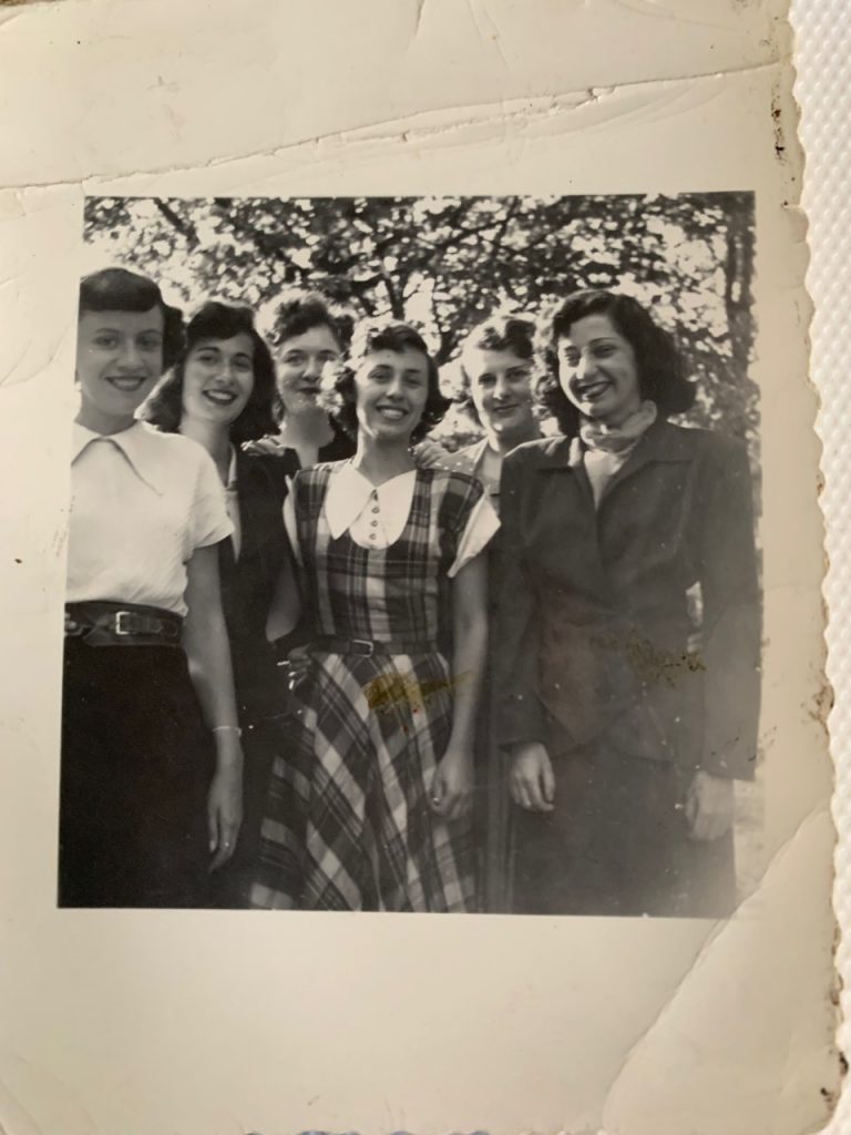 1949 vintage photo of a group of young women posing together in 1940s fashions and 1940s hairstyles. One woman is wearing a 1940s plaid dress and another a two piece women's suit. 