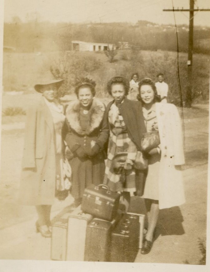 1940s vintage photo of 4 stylish Black Women in very stylish 1940s winter coats and 1940s dresses posing with their suitcases before a trip away. 