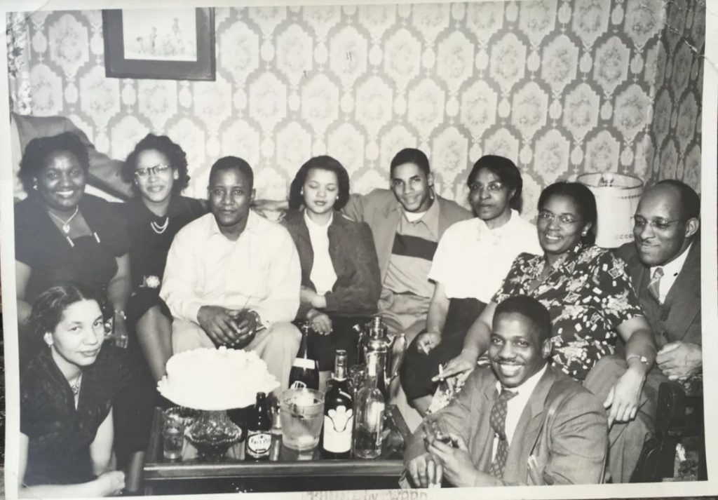 1950s vintage photo of a group of Black Men & Black Women posing for a group shot a birthday party in a living room with funky wallpaper