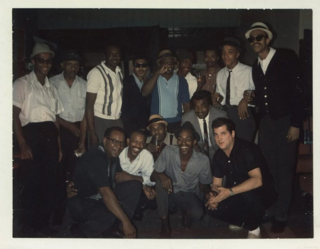 1960s vintage photo of a group of Black Men (and one white man) in 1960s fashions posing together with drinks in hand.