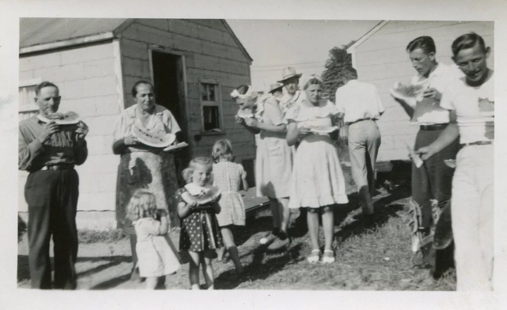 1940s vintage photo of a family enjoying watermelon at picnic / bbq in the summer time. 