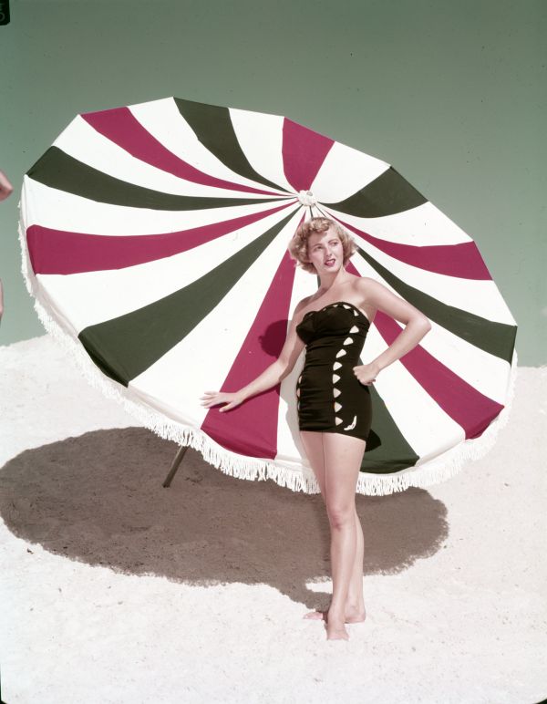 1953 Vintage photo of Harriet Smart modeling Jantzen bathing suit at the beach in front of a giant patio umbrella