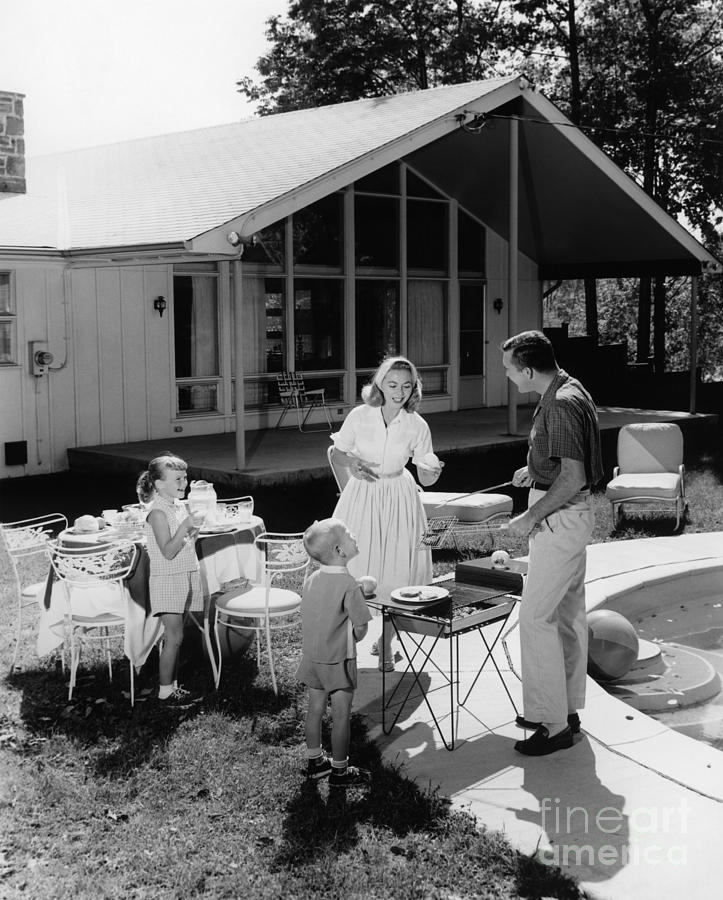 1950s vintage photo of a family grilling hamburgers beside pool in backyard cookout. 