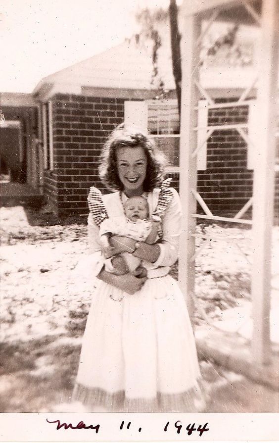 1940s vintage photo of a young mother in a pinafore dress, May 11th, 1944 holding her little child. 