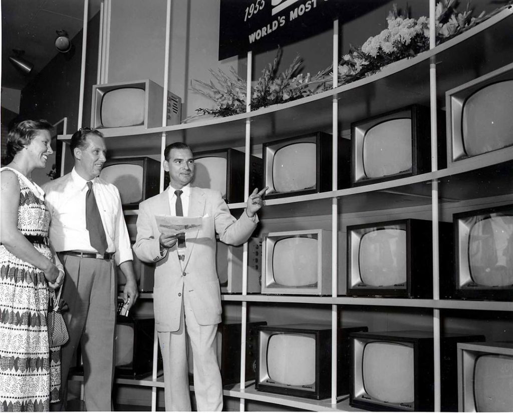 Televisions On Display At The 1950 CNE featuring men in 1950s fashions and a woman in a 1950s dress and purse. 