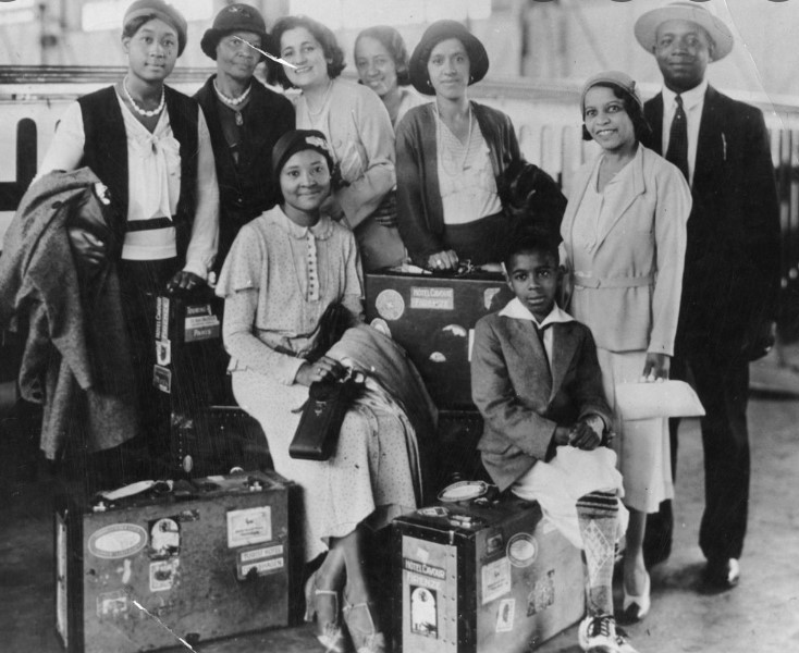 1930s vintage photo of a stylish 1930s Black family in 1930s fashions posing together after two young women returns from their travels. The cousins (Thomas stands at the far left, while Sengstacke is seated at the far left) pose for a family portrait after returning from their trip