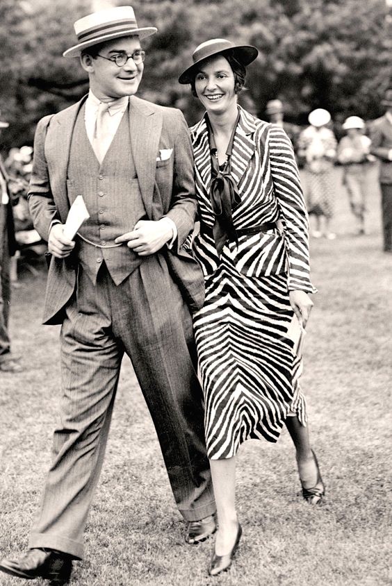 1930s vintage photo of a man and woman in 1930s fashions. The woman is wearing a zebra print 1930s Jacket and matching 1930s skirt. The man is wearing a suit with a straw boating hat. 