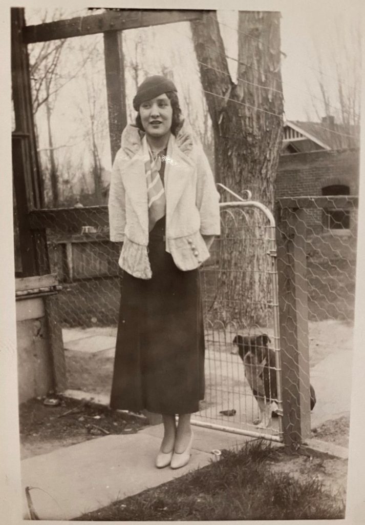 1930s vintage photo of a woman in 1930s fashion posing outside with a dog who is behind the fence. Stunning 1930s street style. 