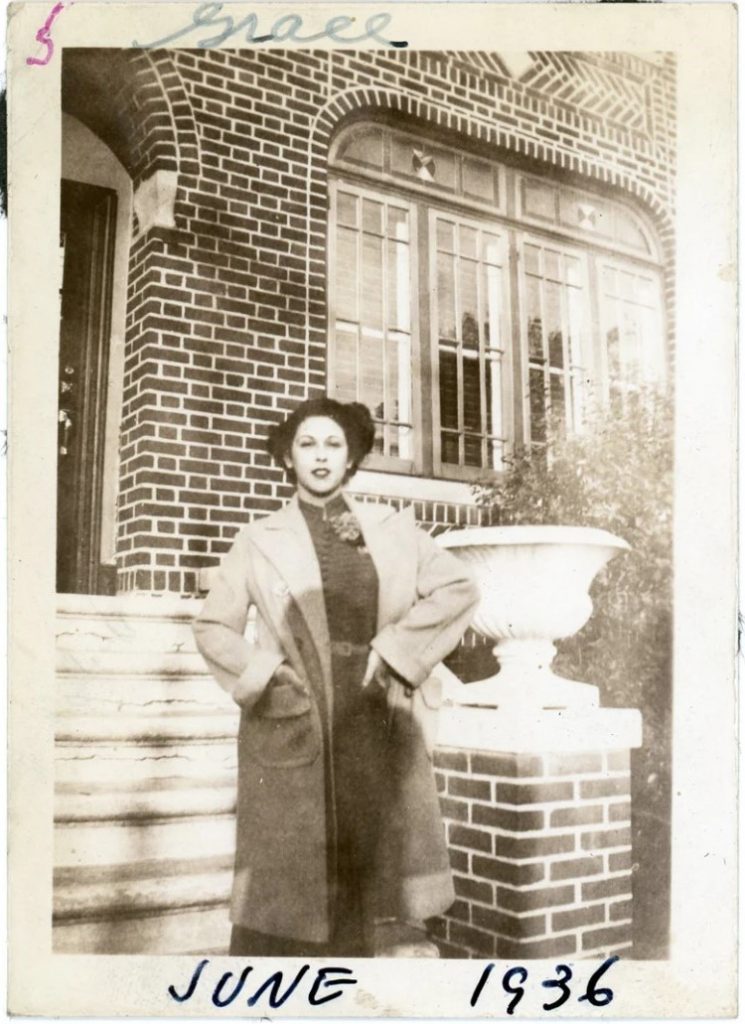 1930s vintage photo of a young woman in a 1930s coat and 1930s dress posing in front of her house. 