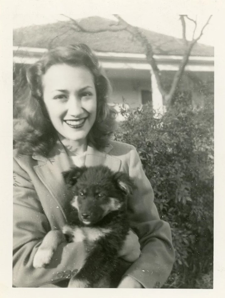 1940s vintage photo of a young woman with a 1940s hairstyle holding a fluffy puppy in her arms. 