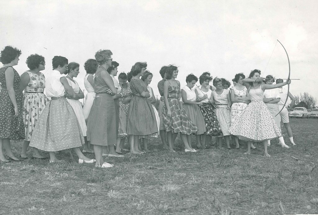 1950s vintage photo of a group of women college students in 1950s dresses and 1950s skirts and blouses trying archery at Palm Beach Junior College