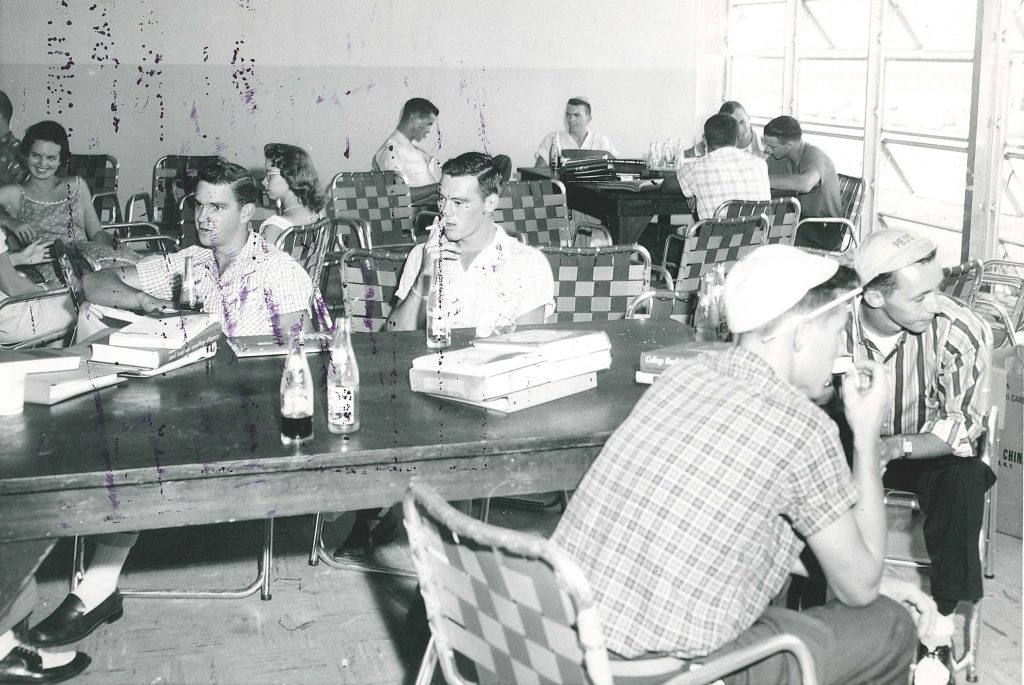 1950s vintage photo of college students taking a break in 1950s fashions. several men are wearing beanies on their head.