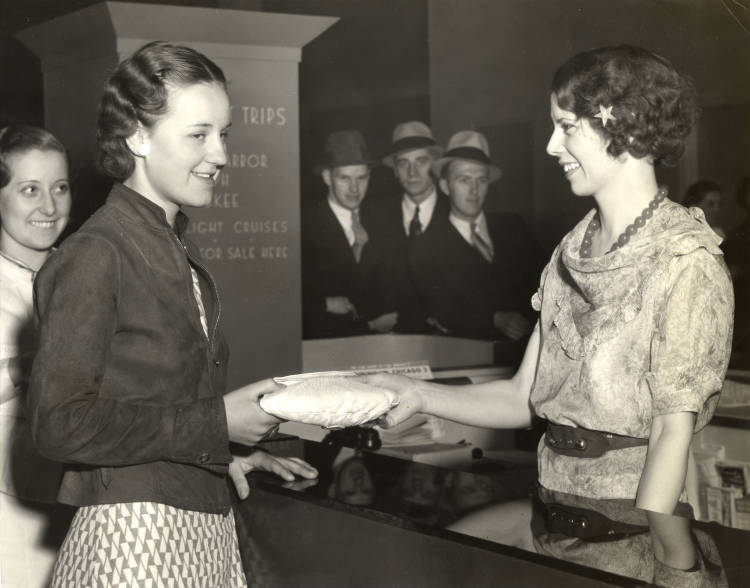 1930s vintage photo of a woman picking up her lost purse from the chicagos World's Fair 1933 1934. The women are wearing 1930s hairstyles and 1930s fashions. 