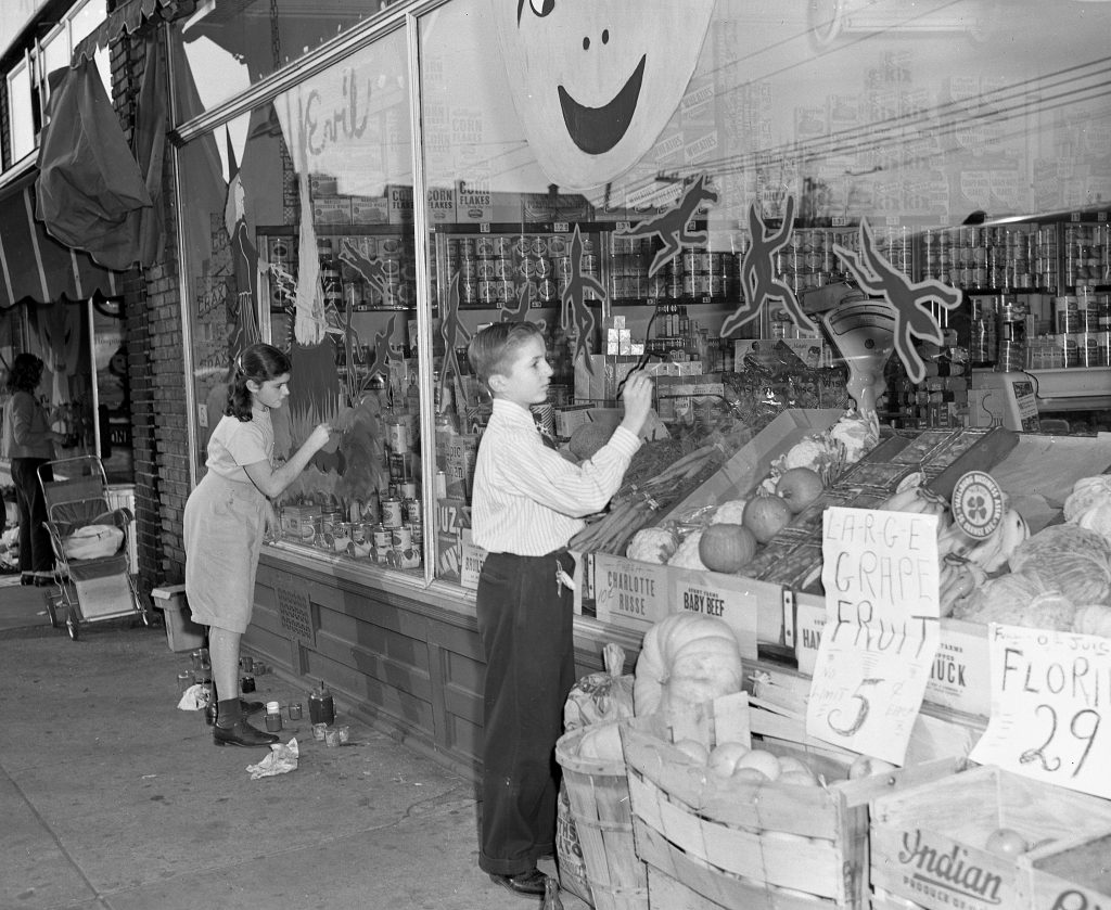 1940s vintage image of two young kids in Newark, NJ painting a Halloween mural on a grocery store window in 1948. 