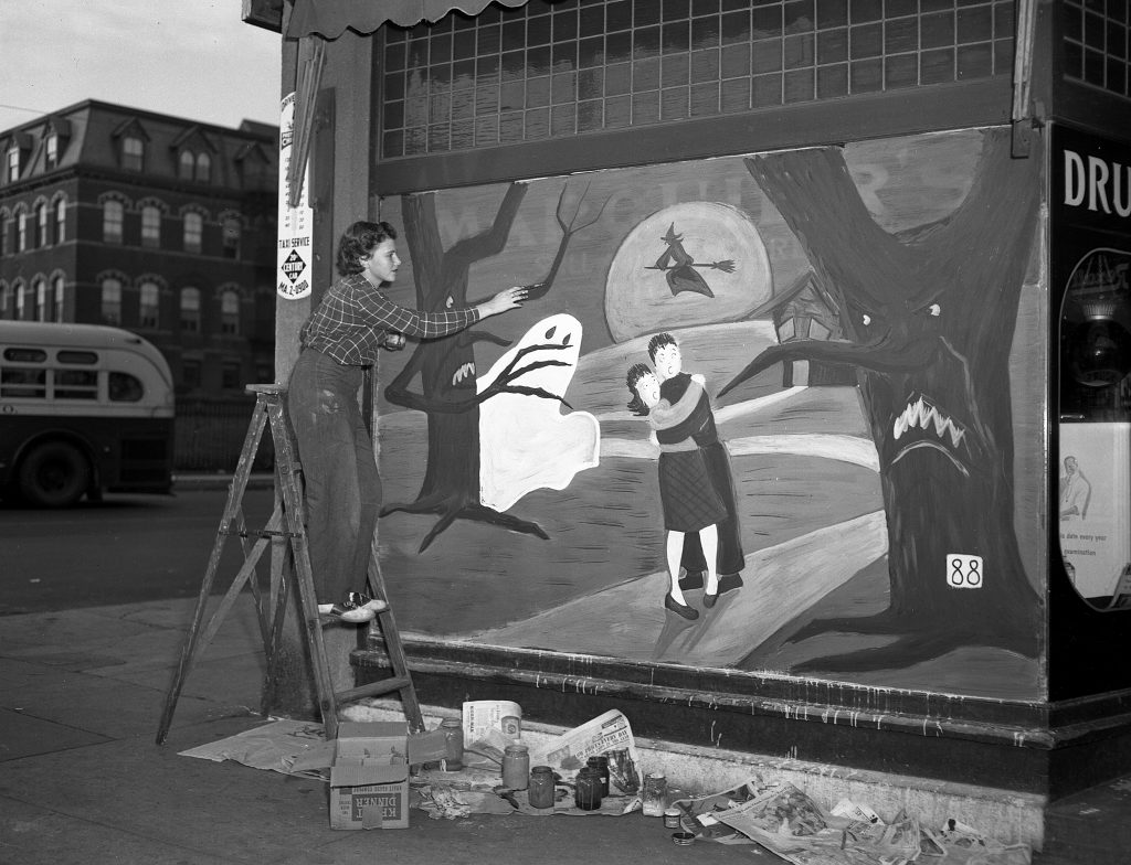 1940s vintage image of a teenage art student in 1948 painting a Halloween scene on a store for Marquier's Pharmacy featuring a Haunted forest. 